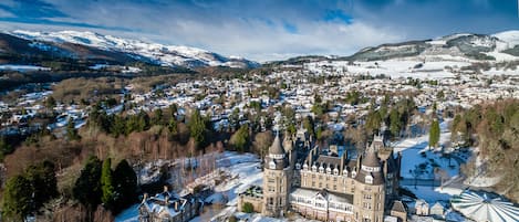 Un castillo histórico con múltiples torres, rodeado por un pueblo con paisajes nevados y montañas al fondo.