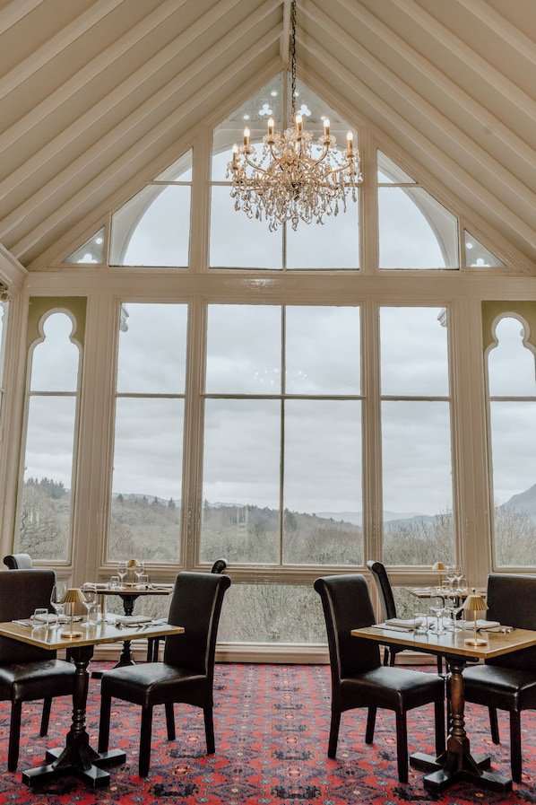 A dining room with a large window, a chandelier, and a red carpet.