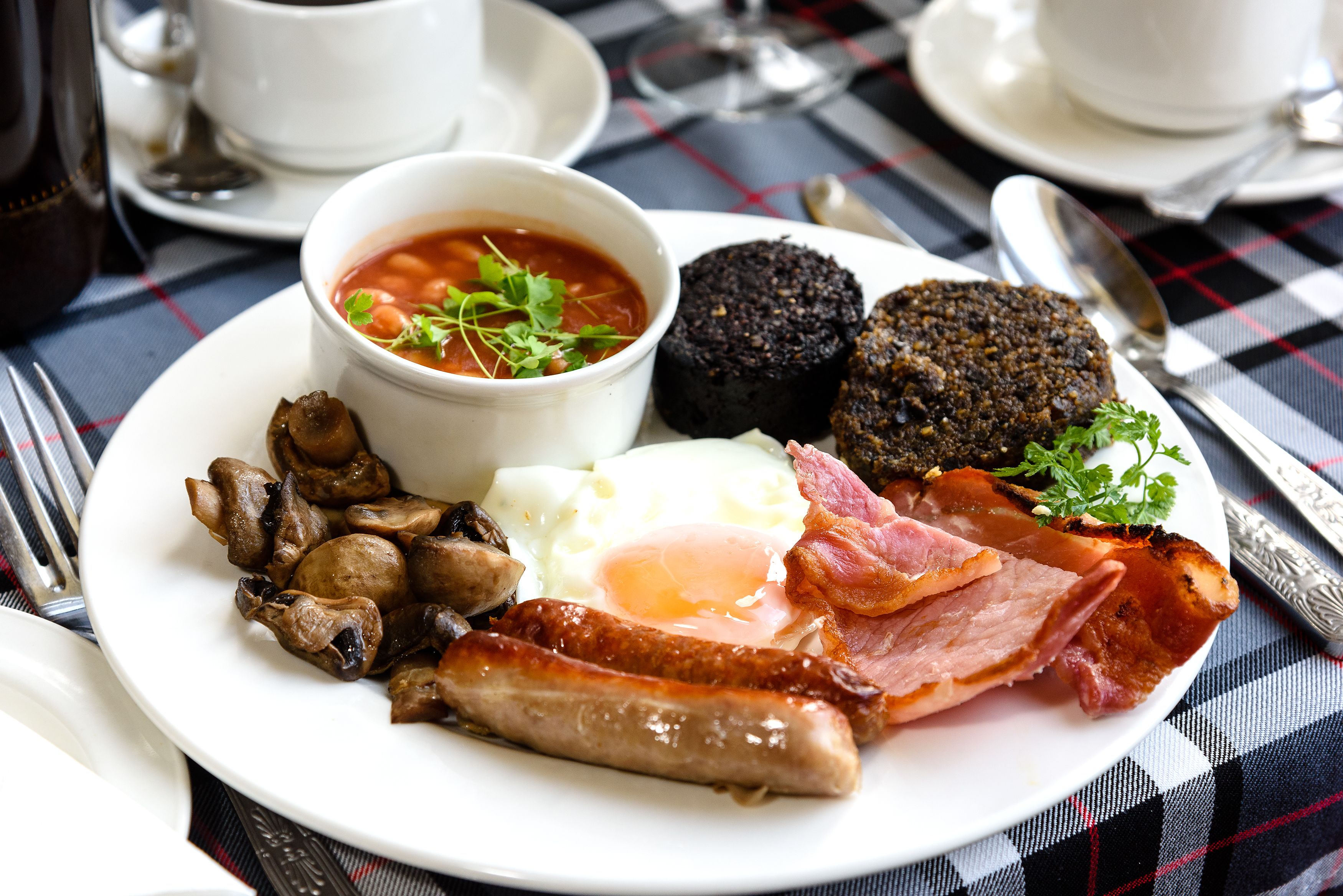 Un plato de desayuno con huevos, tocino, salchichas, champiñones, morcilla y un bol de sopa.