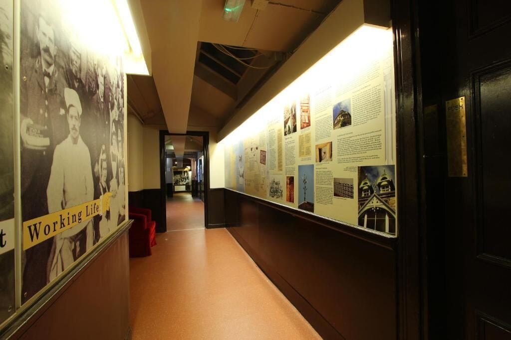 A hallway with informational posters on the walls, a carpeted floor, and a door with a push button.