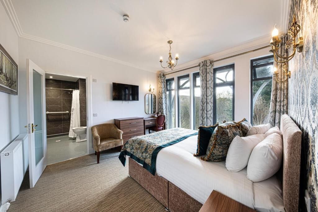 A bedroom with a large bed, a desk, a chair, a television, and a bathroom with a shower and toilet.