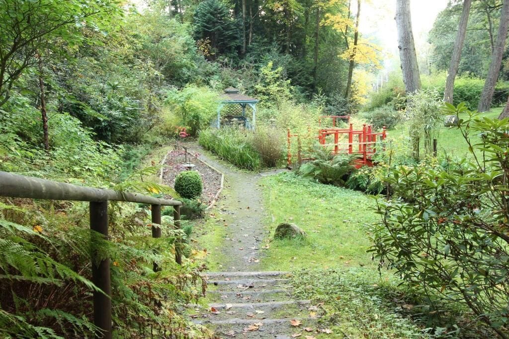 A garden pathway with a gazebo, a red gate, and a stone staircase.