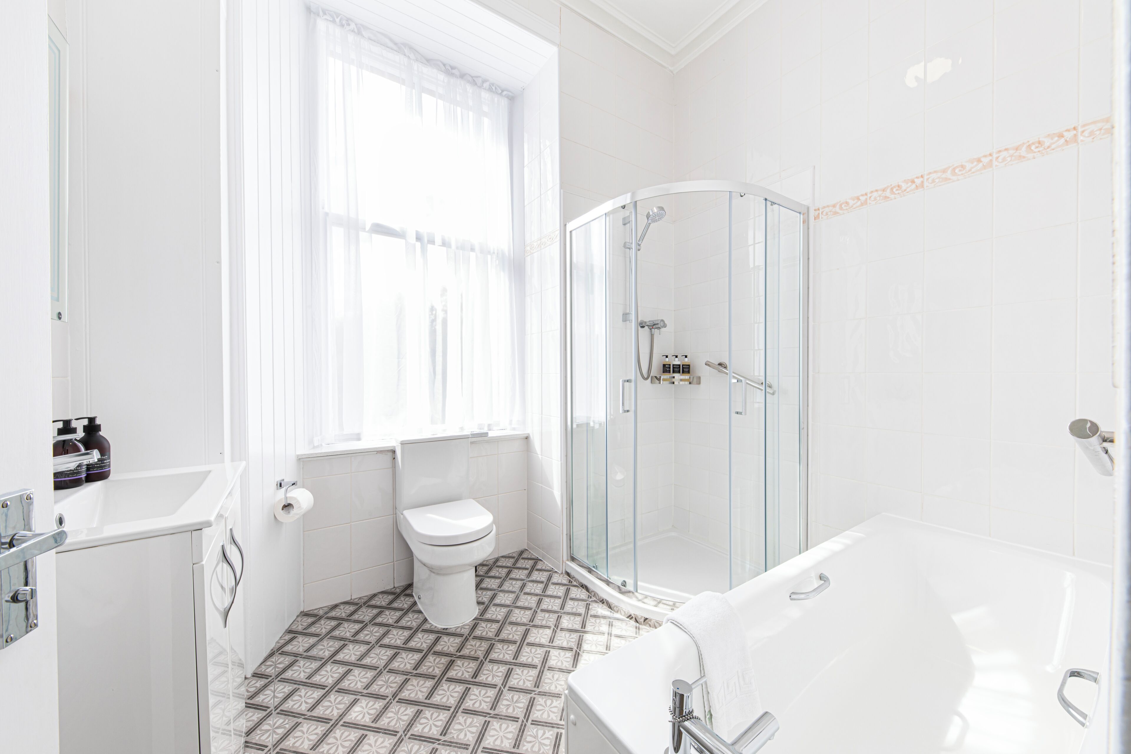 A modern bathroom with a glass-enclosed shower, a white bathtub, and a patterned floor.