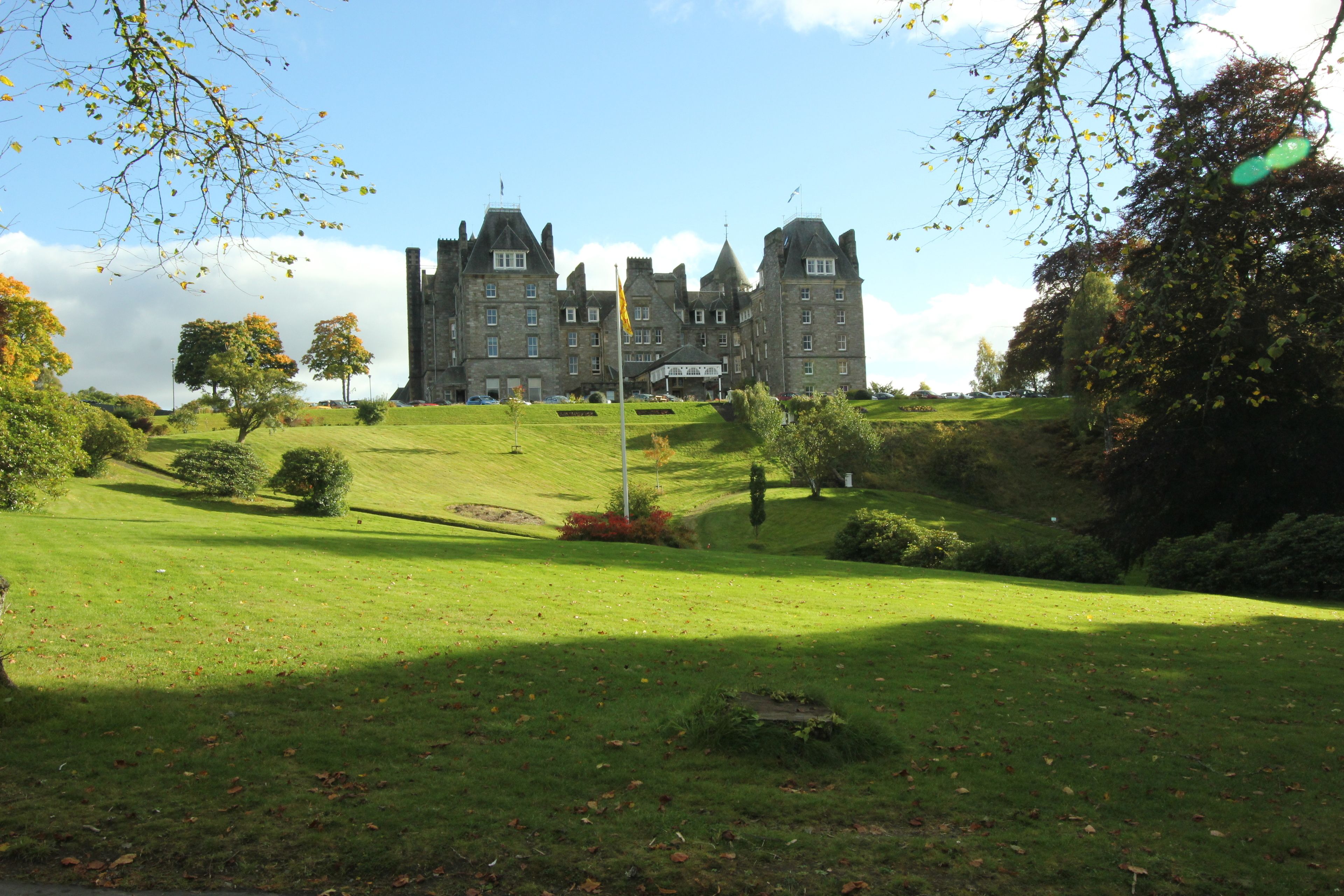 A large, historic building with multiple towers and a well-maintained lawn in front.