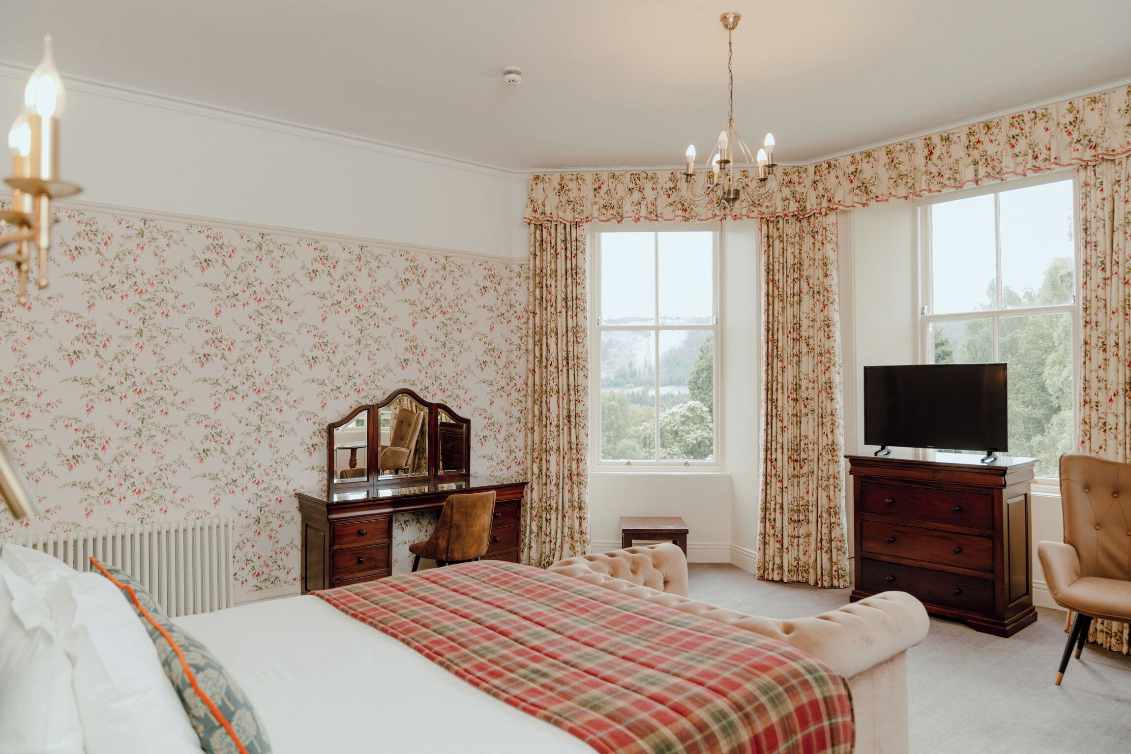 A bedroom with a bed, a dresser, a television, and a window with curtains.