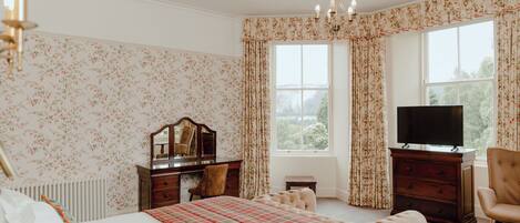 A bedroom with a bed, a dresser, a television, and a window with curtains.