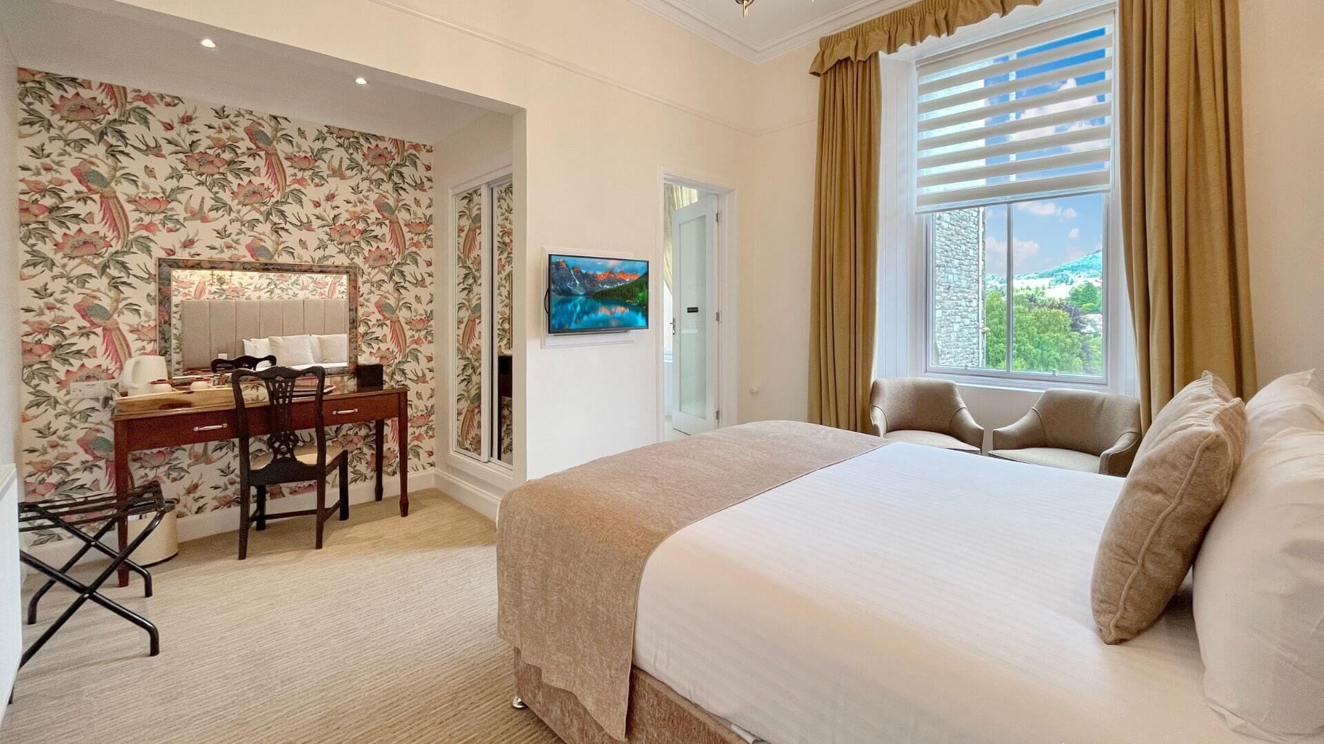 Een hotelkamer met een groot bed, een bureau met stoel, een televisie en een raam met gordijnen.