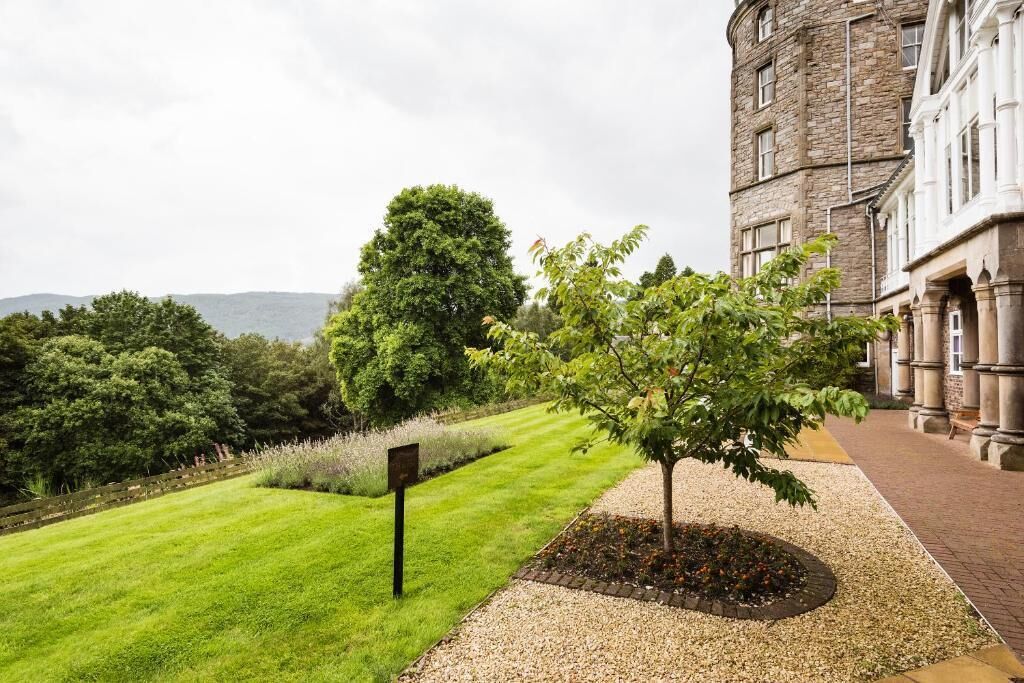 Un césped bien cuidado con un árbol pequeño, un camino de grava y un edificio de piedra con arquitectura clásica.