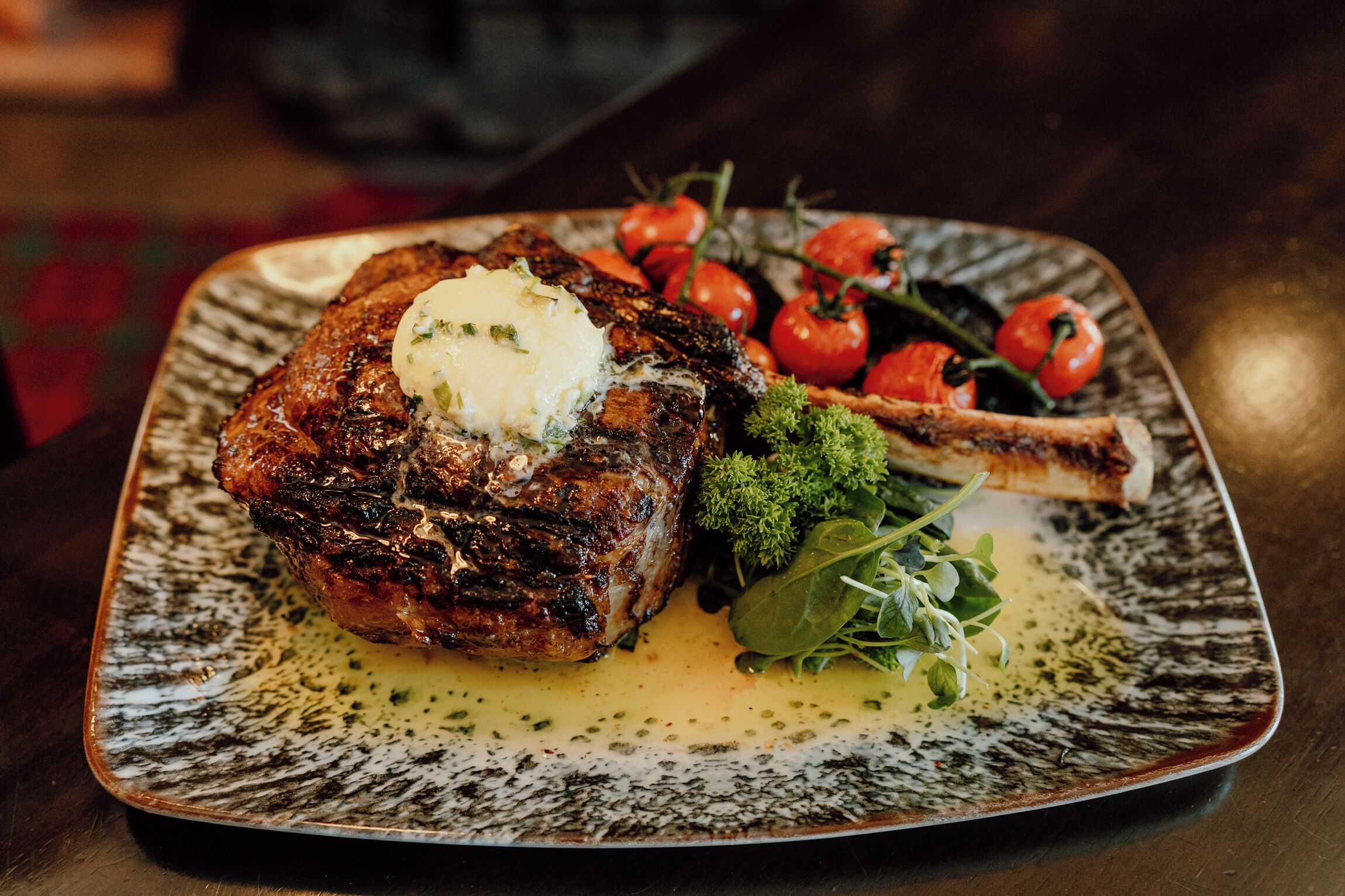 Bife com um pedaço de manteiga por cima, acompanhado de tomates cereja e vegetais em um prato de cerâmica.