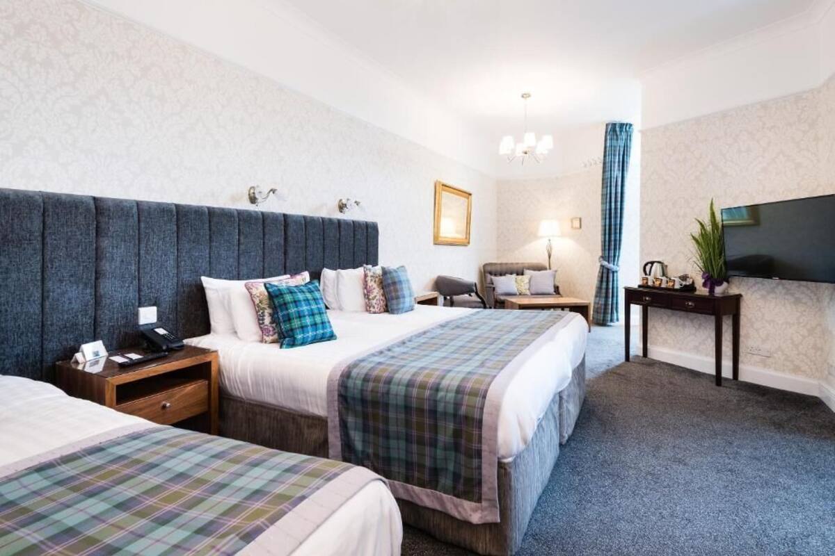 Une chambre d’hôtel avec deux lits, un bureau, une chaise, une télévision et une lampe.