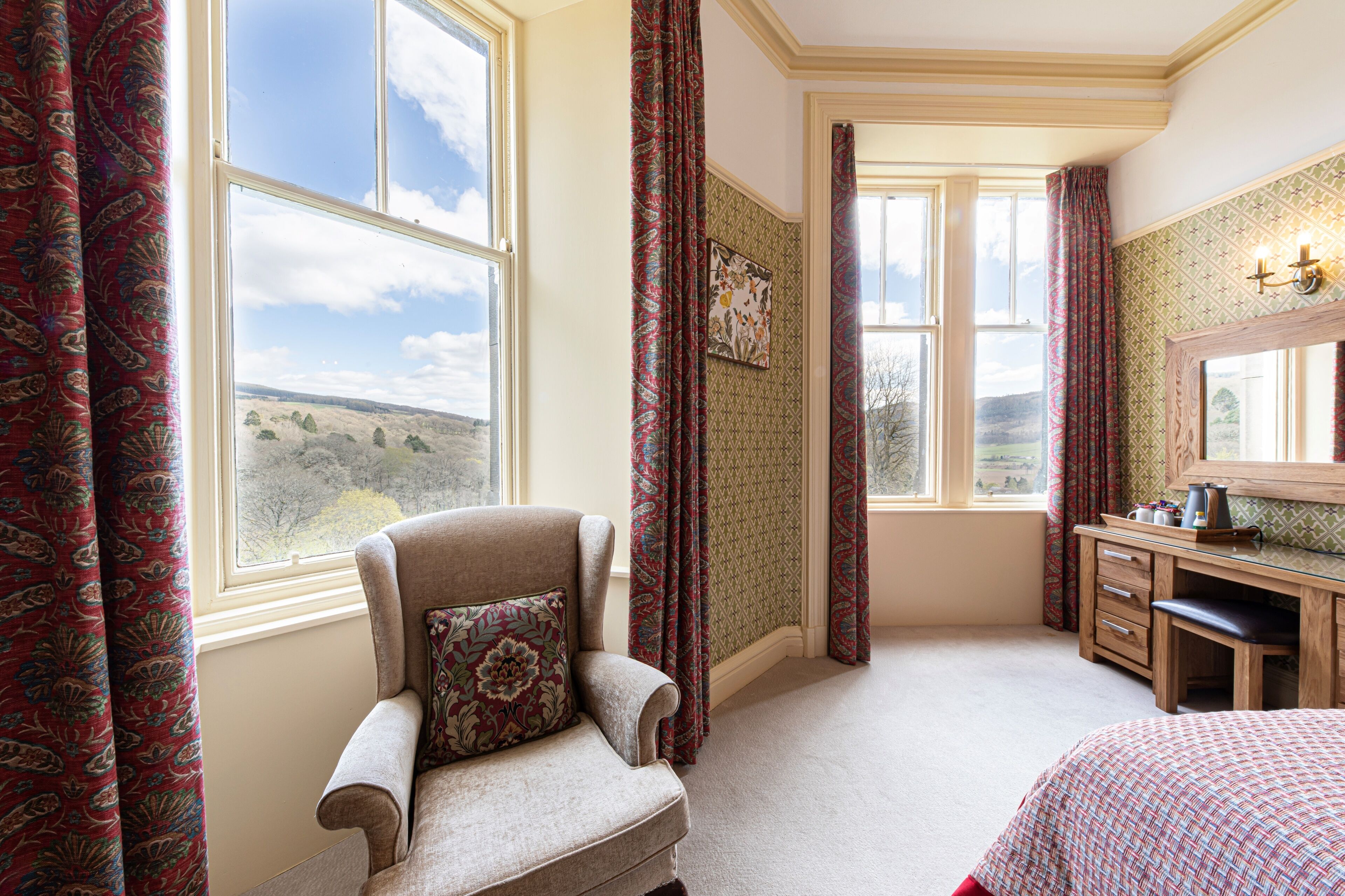A bedroom with a large window, a chair, a desk, and a bed.
