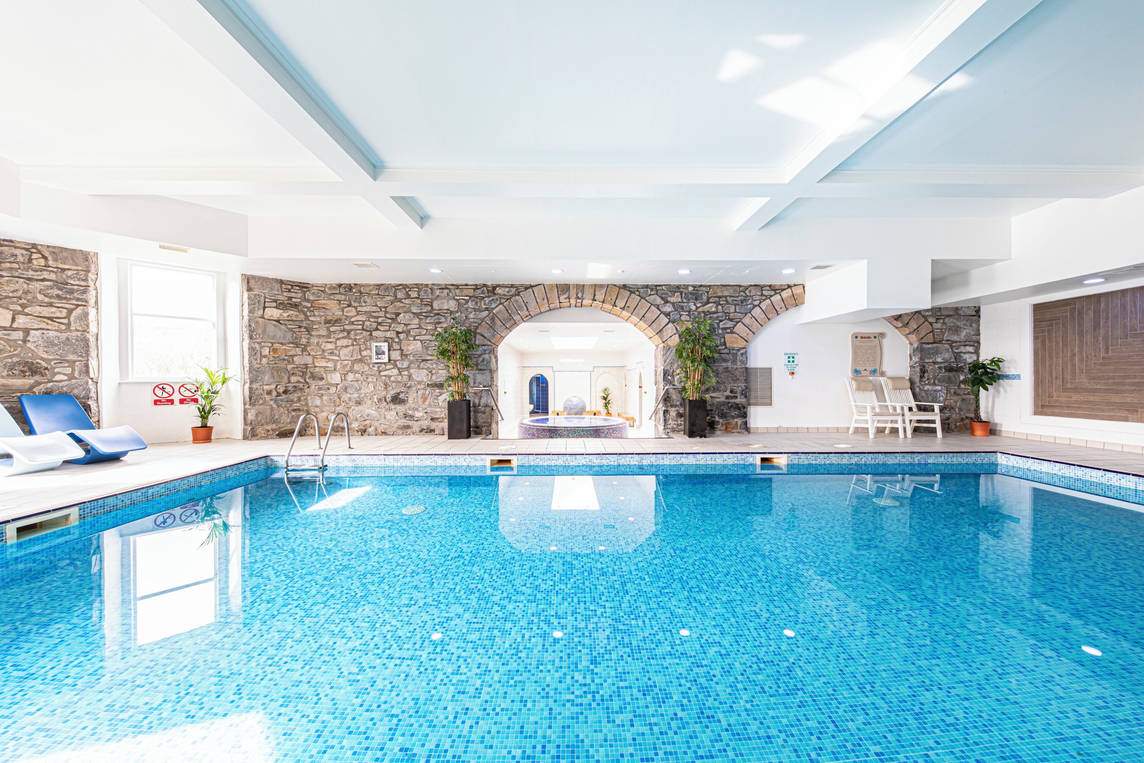 Una piscina interior amb aigua blava cristal·lina, parets de pedra i una arcada de pedra que condueix a una porta.