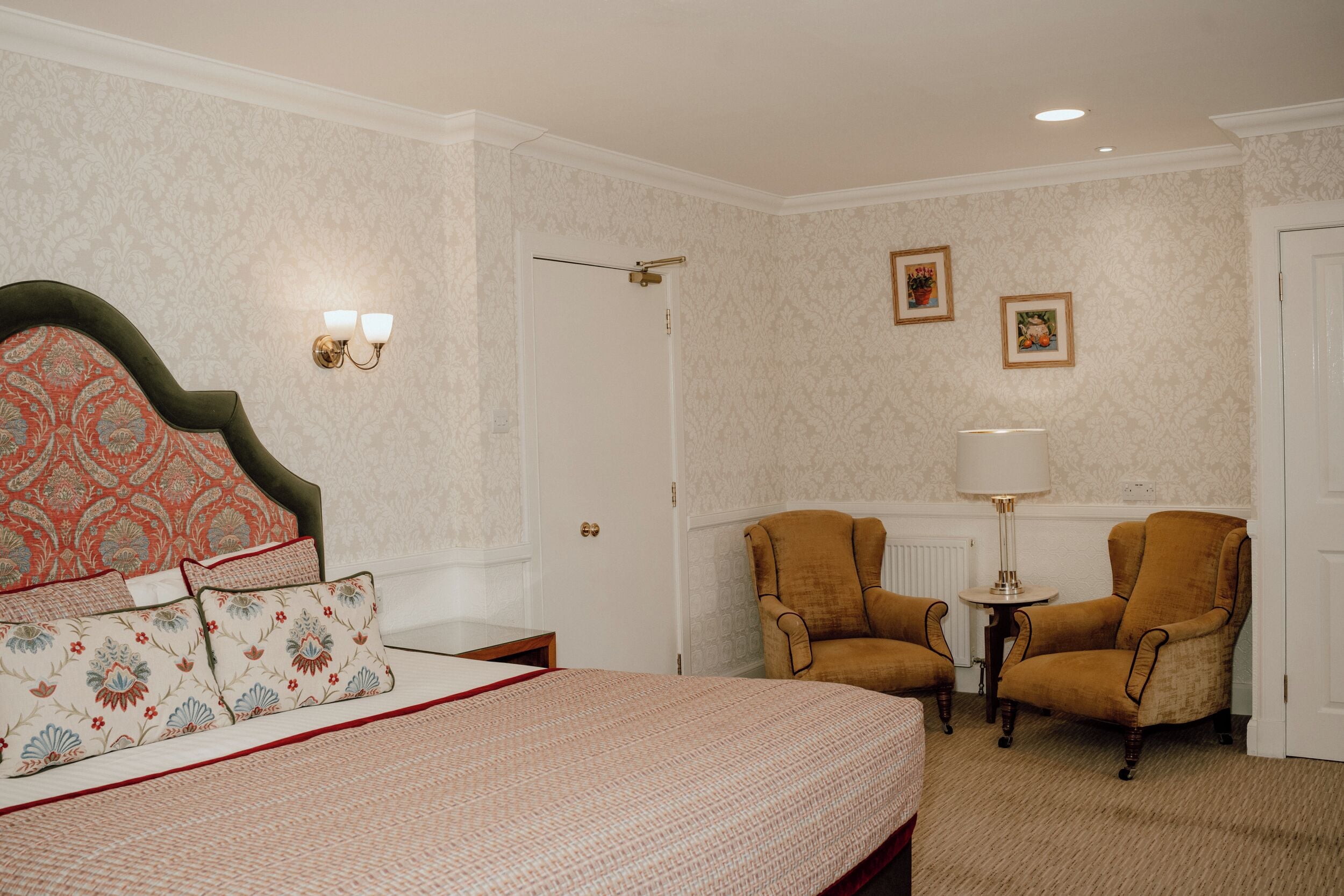 Une chambre à coucher avec un lit, deux fauteuils, une petite table et une lampe.