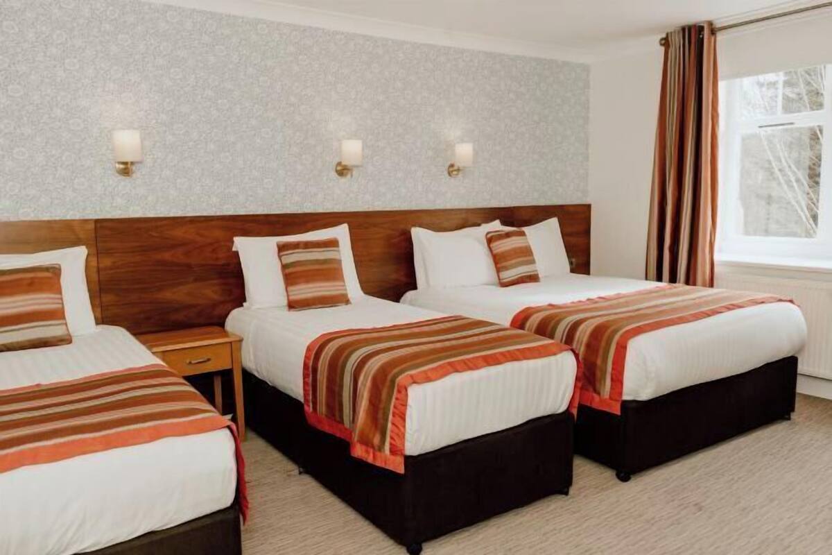 Une chambre d’hôtel avec deux lits, une tête de lit en bois, des tables de chevet et une fenêtre avec des rideaux.