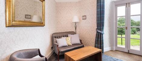A room with a sofa, a chair, a wooden table, a mirror, a lamp, and a view through a door.