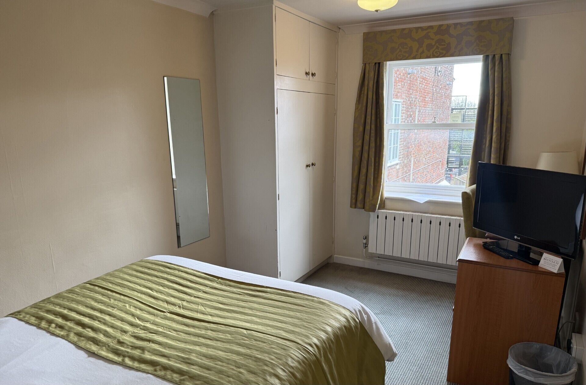 A hotel room with a bed, a television, a wardrobe, and a window with curtains.