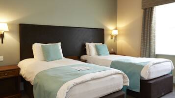A hotel room with two beds, each with a headboard, bedside lamps, and a window with curtains.