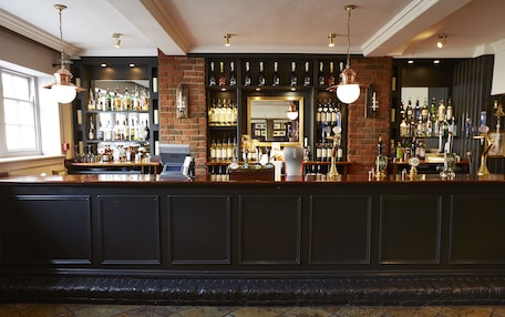 A bar area with a brick wall, shelves of liquor bottles, and hanging light fixtures.