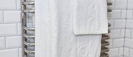 Una toalla blanca colgada en un toallero metálico en un baño con paredes de azulejos blancos.