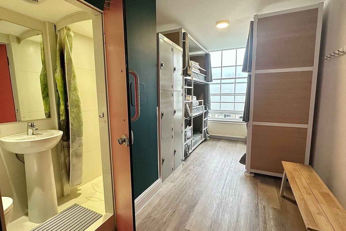 A narrow hallway with a bathroom on the left, a wardrobe with hanging clothes, and a bench on the right.