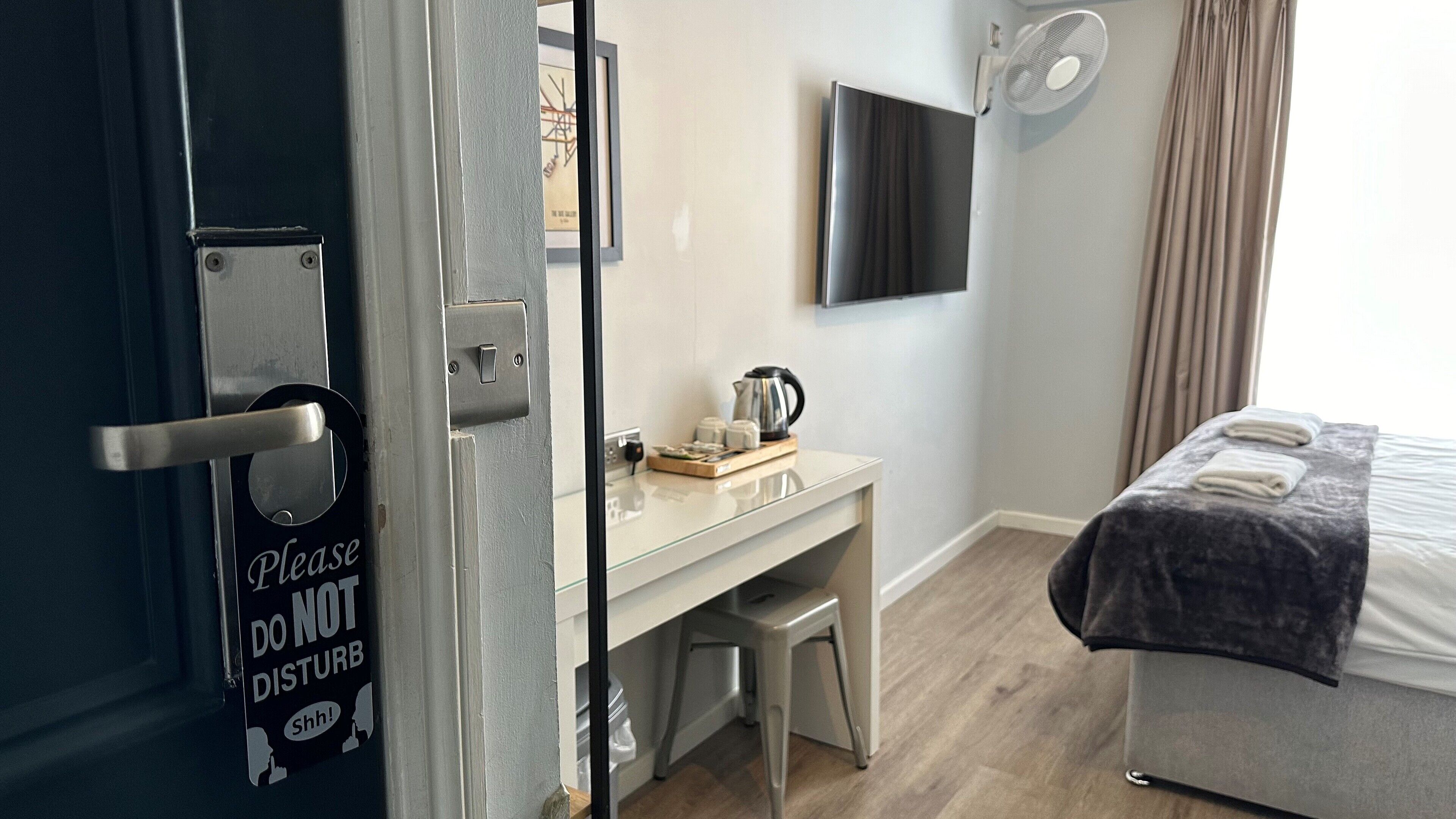 Une chambre d’hôtel avec un lit, un bureau doté d’une bouilloire, un téléviseur fixé au mur et une porte sur laquelle est apposée une pancarte indiquant : « Veuillez ne pas déranger ».