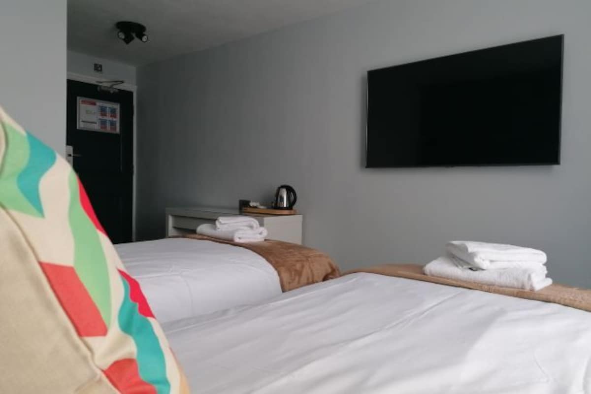Hotelkamer met twee bedden, een flatscreen televisie aan de muur, een bureau met waterkoker en een deur met een bordje.