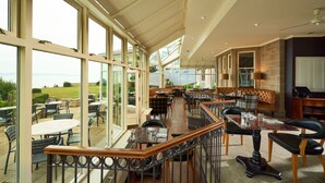 Un amplio comedor interior con ventanas grandes, una escalera de madera y vistas al exterior.