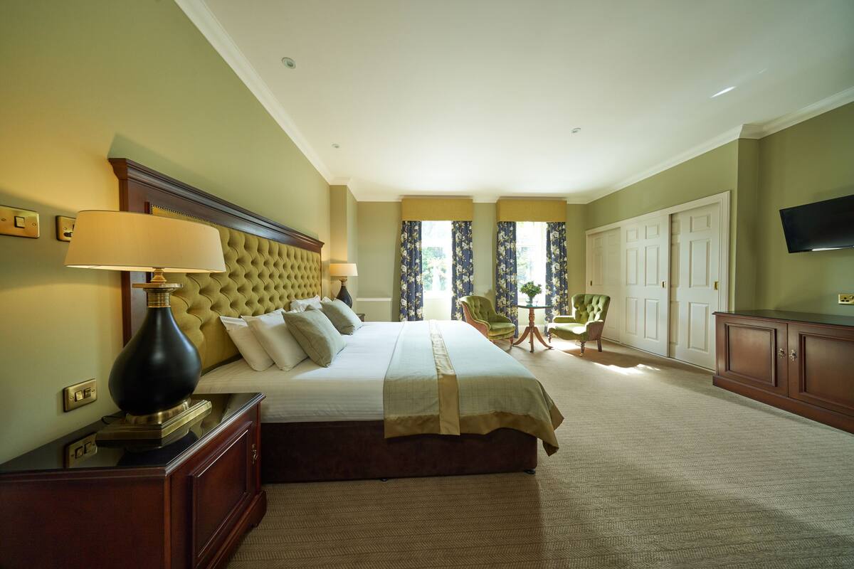 A hotel room with a large bed, a television, a desk with a lamp, and a chair.