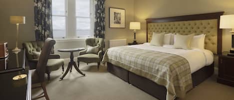 A hotel room with a large bed, two armchairs, a small table, and a window with curtains.