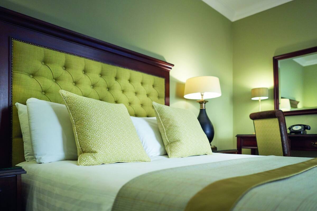 A hotel room with a tufted headboard, a bed with white and patterned pillows, a bedside lamp, and a nightstand with a telephone.