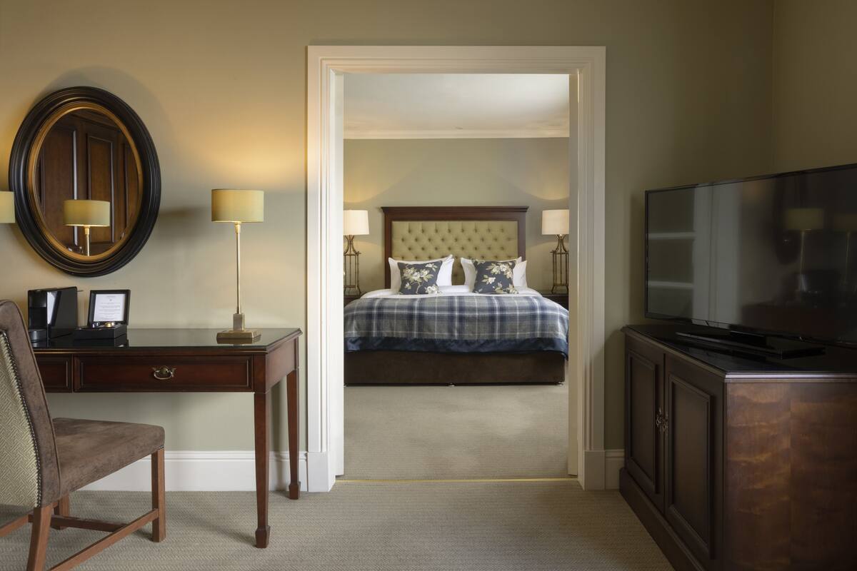 A hotel room with a bed, a desk, a chair, a television, and a mirror.