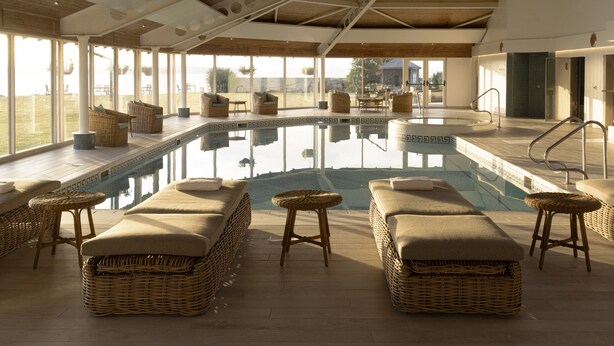 Un área de piscina interior moderna con mobiliario de mimbre y vistas al exterior.