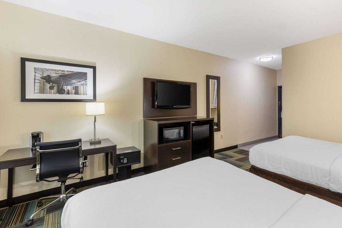 A hotel room with a bed, a desk with a chair, a television, a microwave, and a framed picture on the wall.