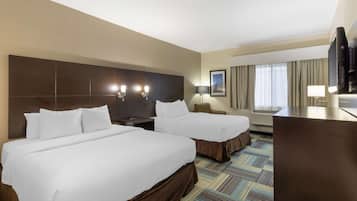 A hotel room with two beds, a desk, a TV, and a large window with curtains.