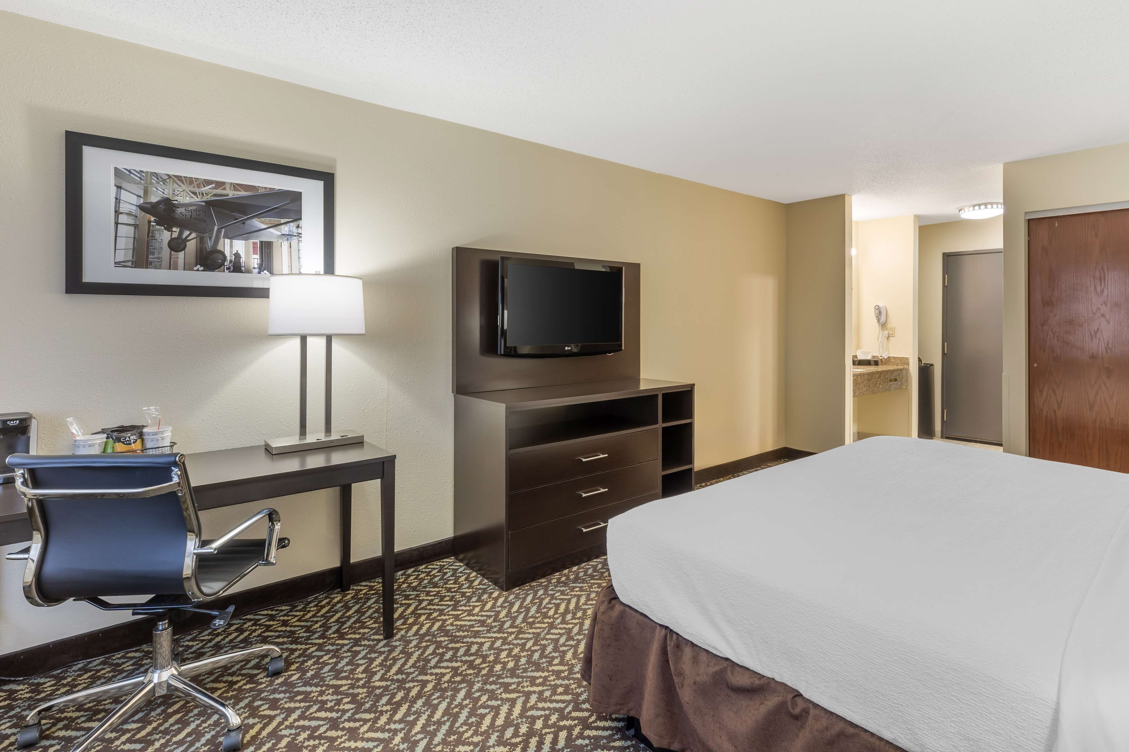 A hotel room with a bed, desk, chair, television, and a framed picture on the wall.