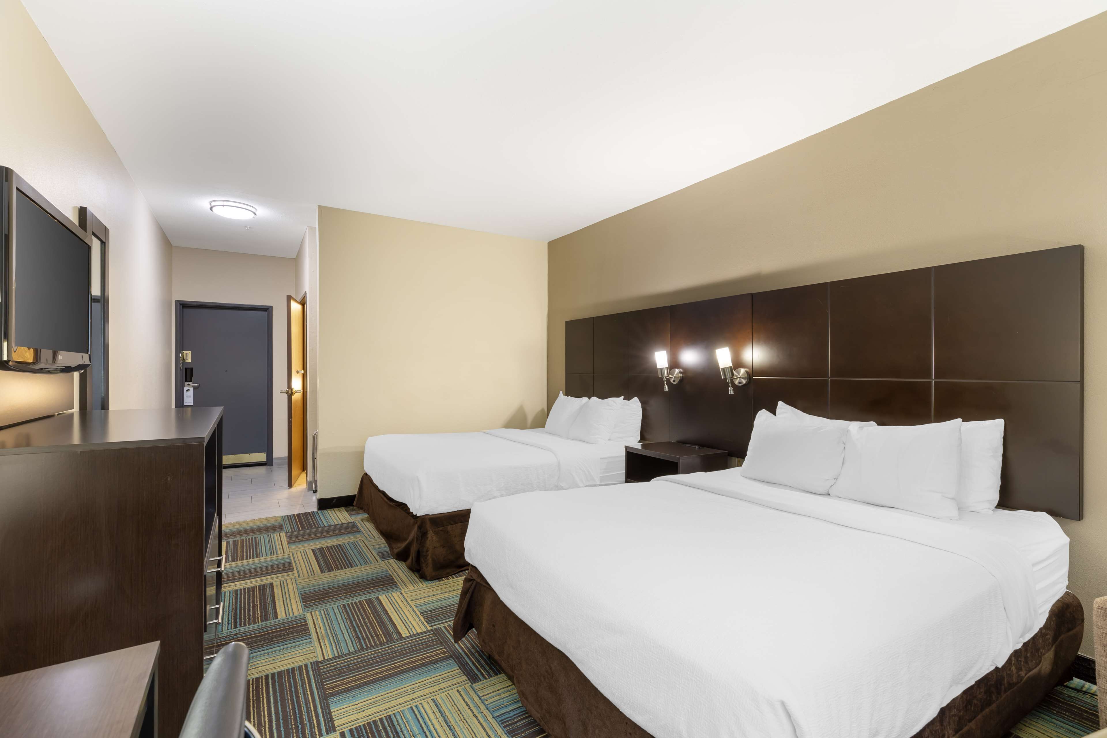 Ein Hotelzimmer mit zwei Betten, einem Schreibtisch, einem Fernseher und einem gemusterten Teppich.