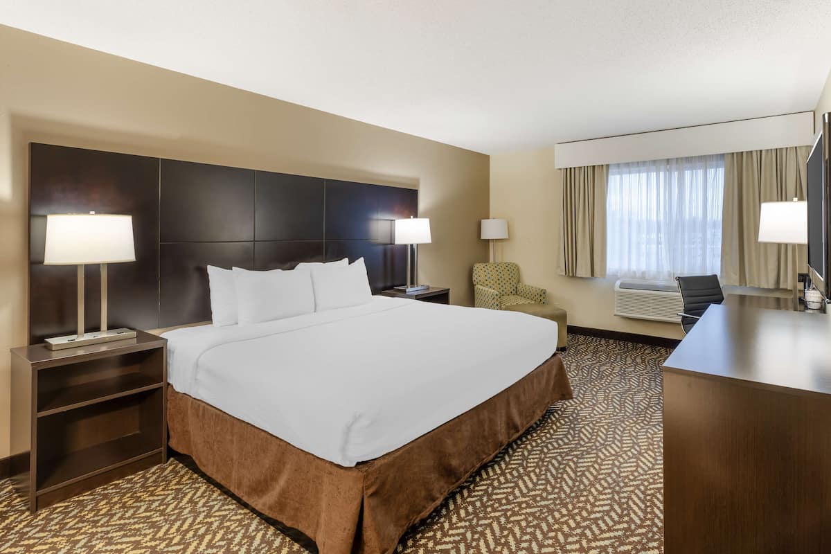 A hotel room with a large bed, two bedside lamps, a desk, a chair, and a large window with curtains.