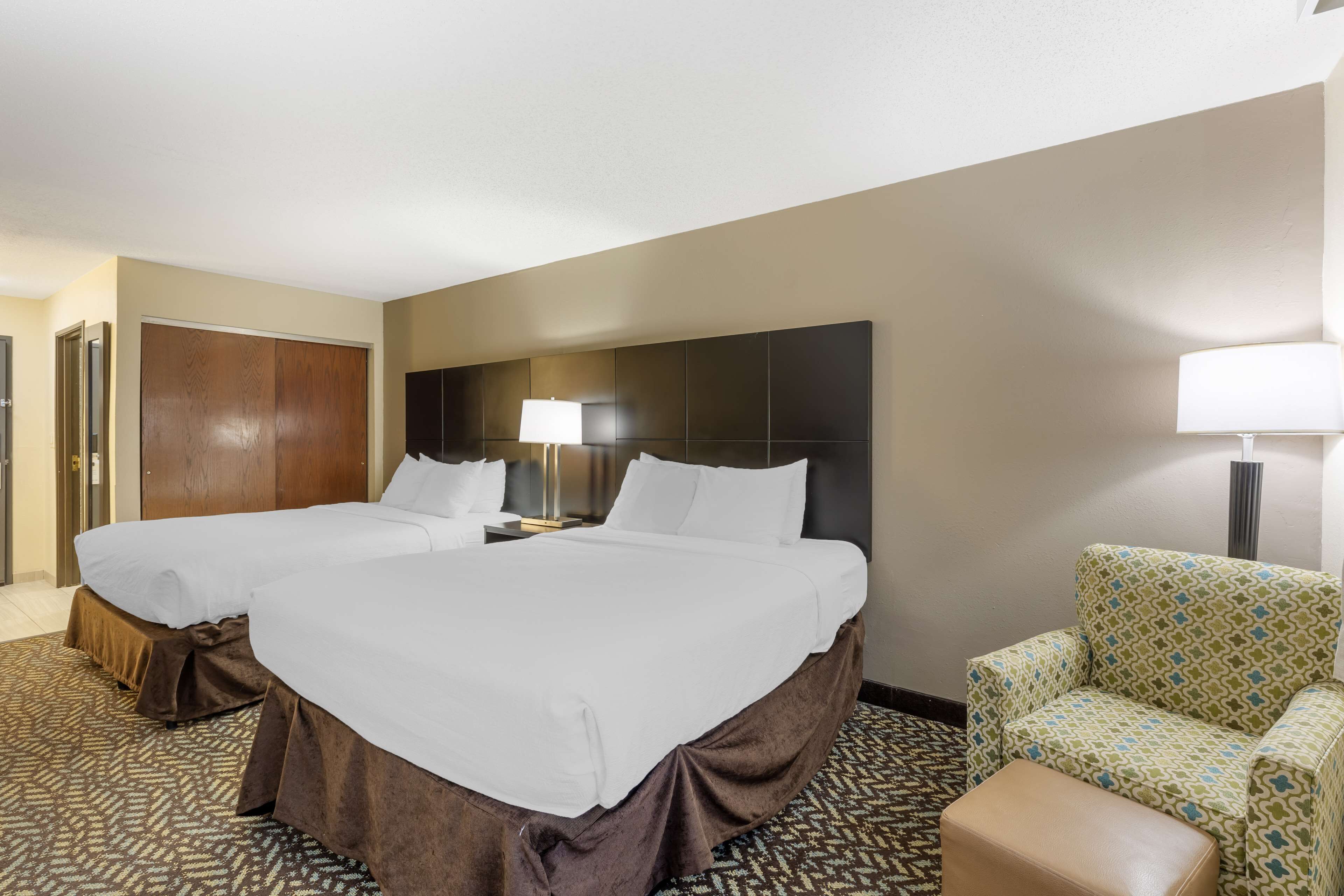 Quarto de hotel com duas camas, um sofá, uma poltrona e um abajur.