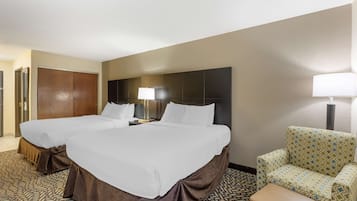 Quarto de hotel com duas camas, um sofá, uma poltrona e um abajur.