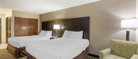A hotel room with two beds, a sofa, a chair, and a lamp.