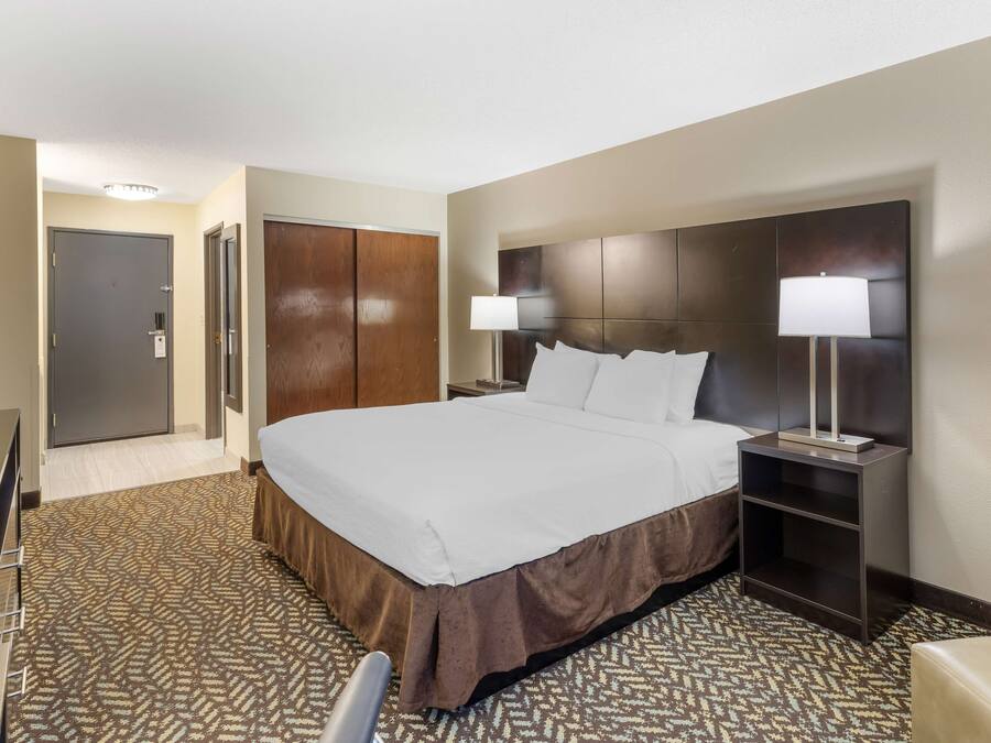 Una habitación de hotel con una cama grande, un escritorio, un armario y una mesita de noche con lámpara.