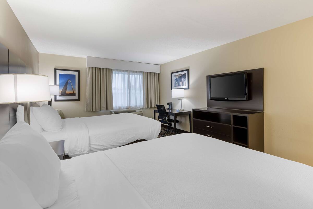 A hotel room with two beds, a desk with a chair, a television, and a window with curtains.