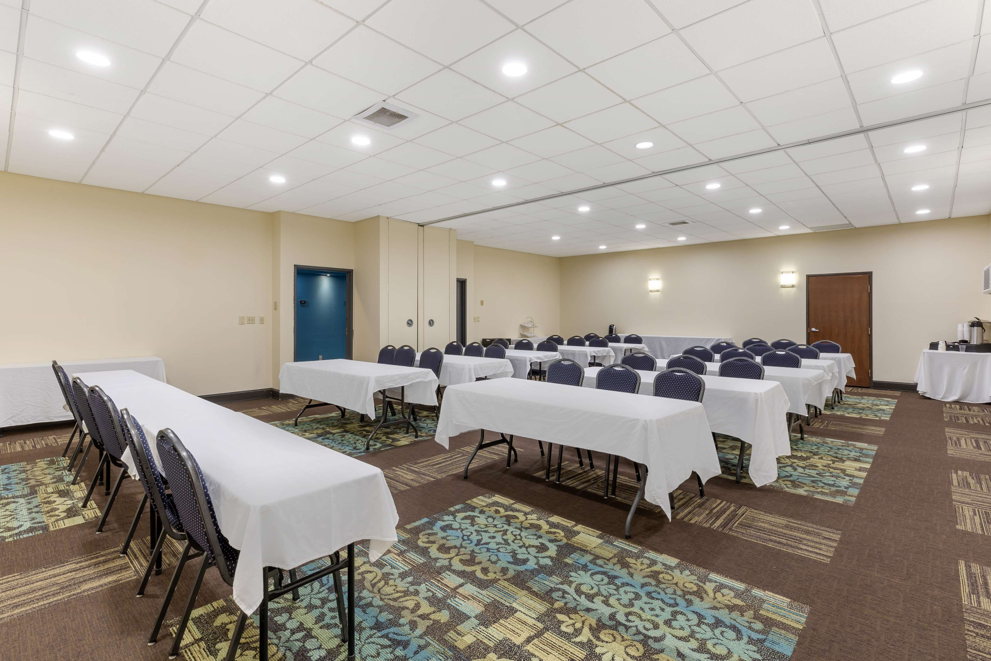 A conference room with multiple tables and chairs, carpeted floors, and a ceiling with recessed lighting.