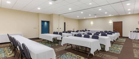 A conference room with multiple tables and chairs, carpeted floors, and a ceiling with recessed lighting.