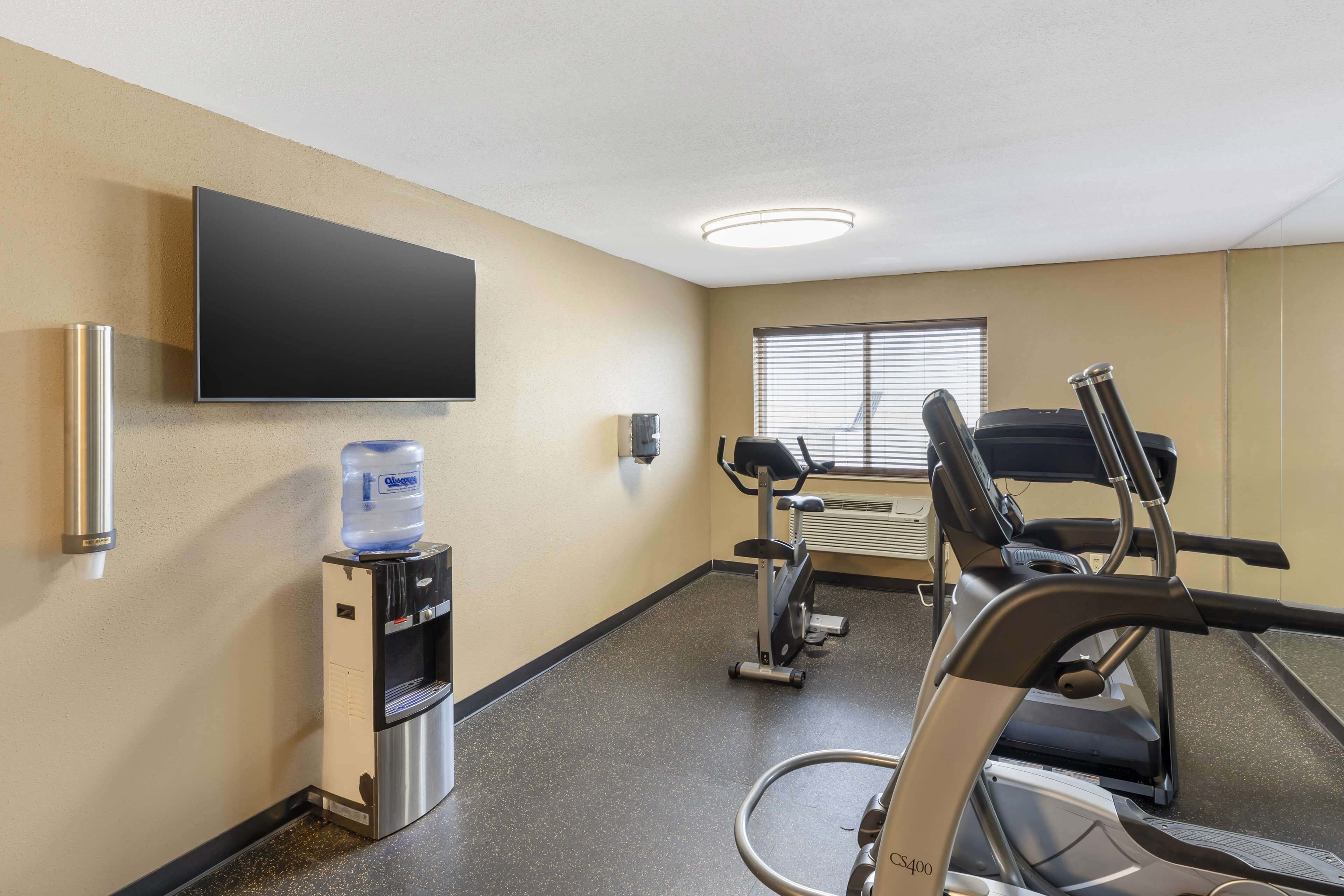 A fitness room with a water dispenser, a television, and exercise equipment.