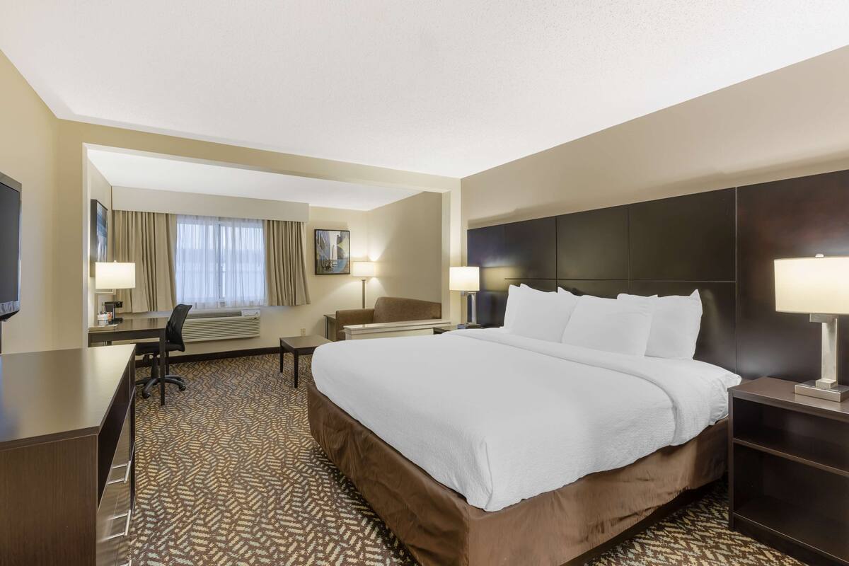 A hotel room with a large bed, a desk, a chair, a TV, and a window with curtains.