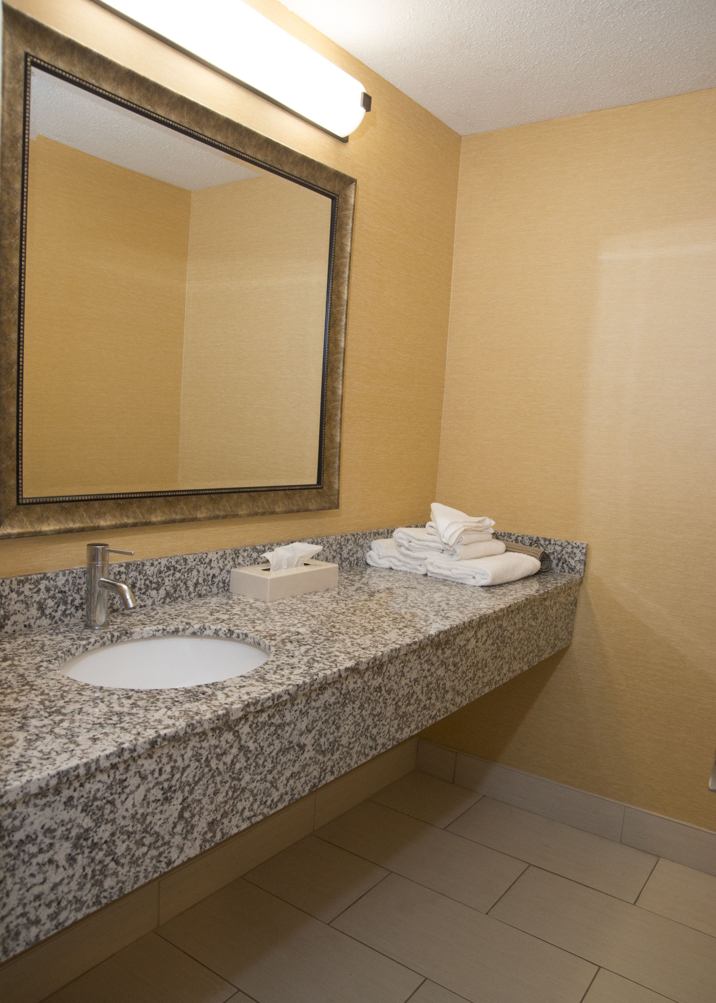 A bathroom with a granite countertop, a sink, a mirror, and a towel rack.