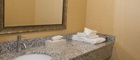 A bathroom with a granite countertop, a sink, a mirror, and a towel rack.