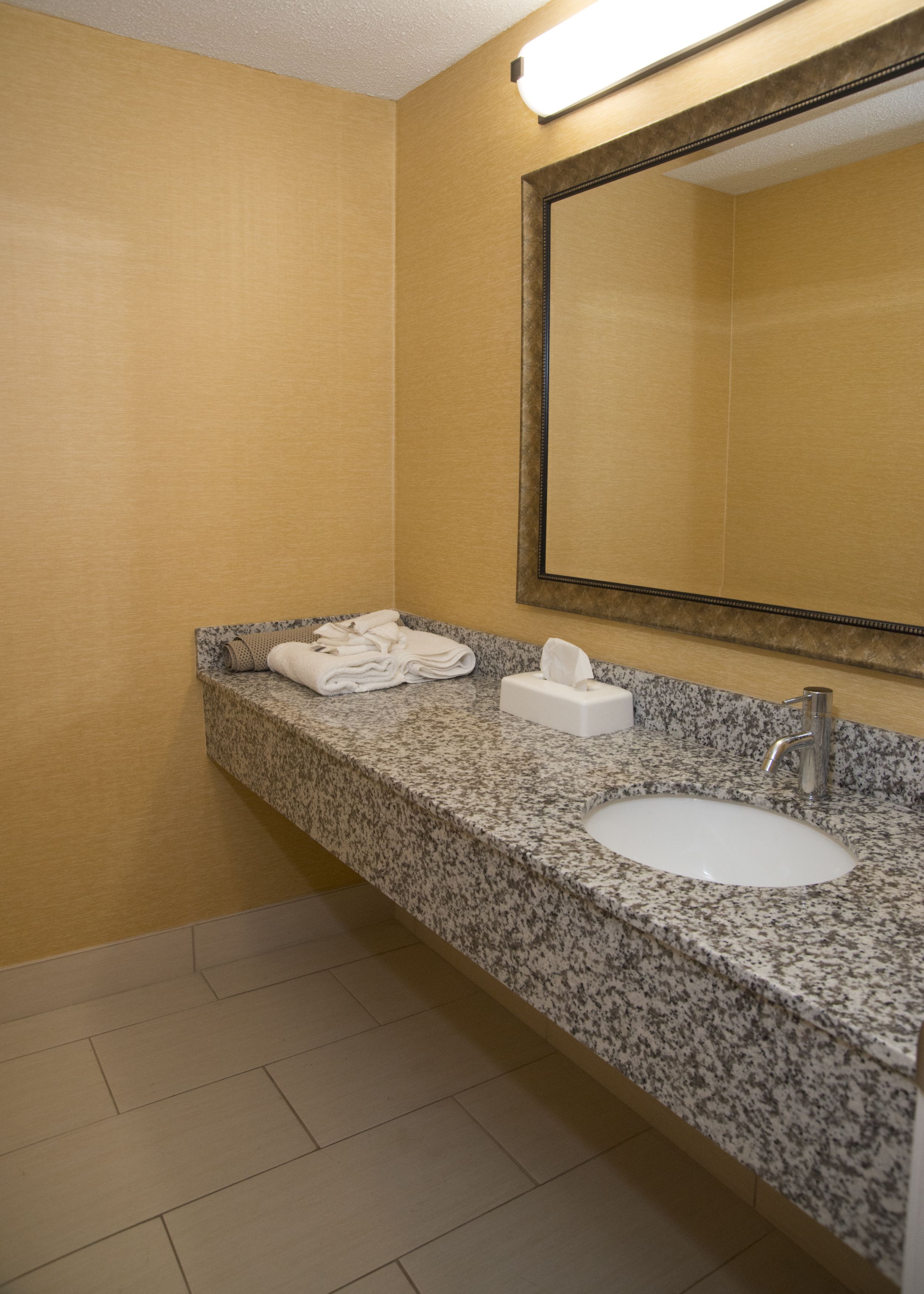 A bathroom with a granite countertop, a sink, a mirror, and a towel dispenser.