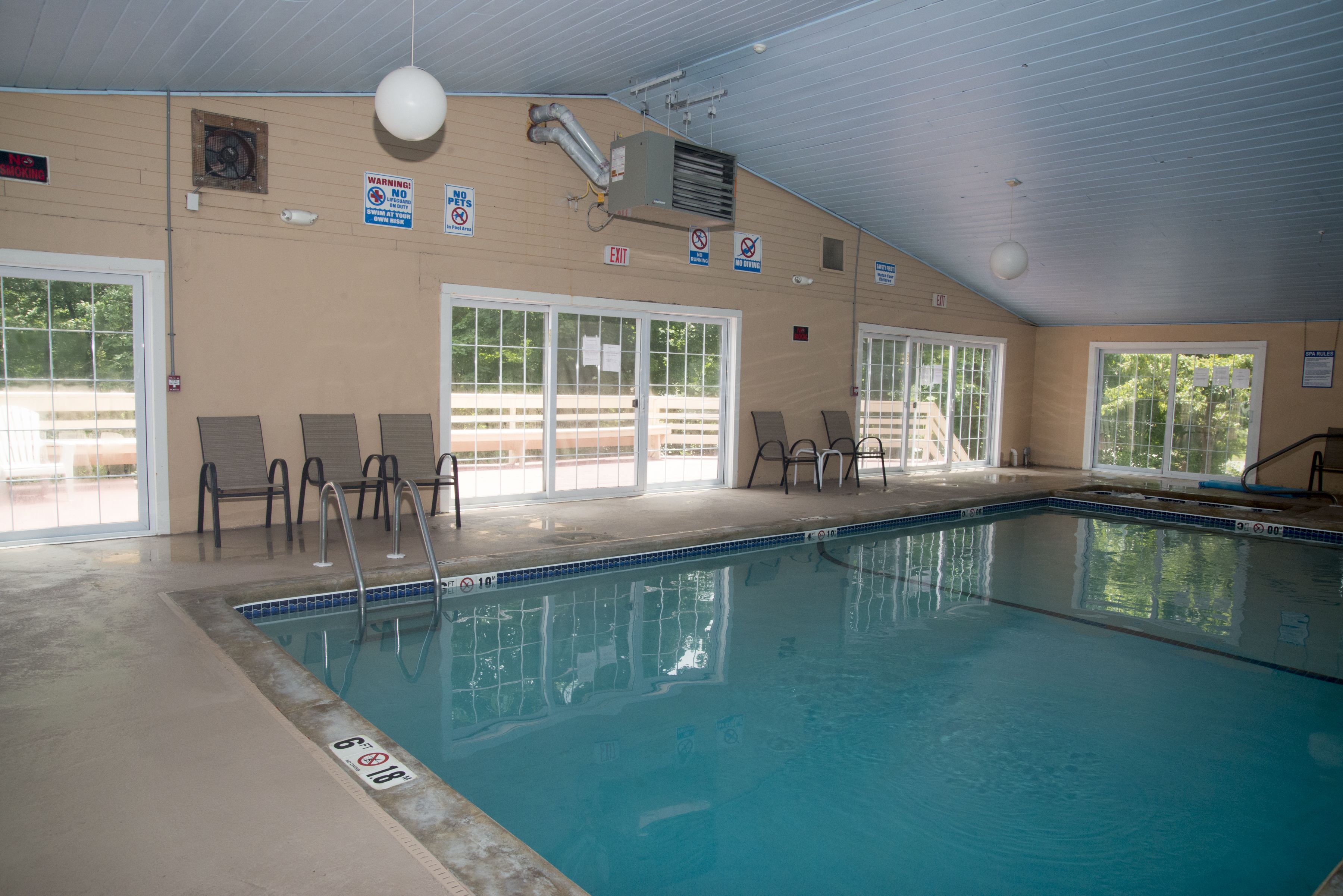 An indoor swimming pool with clear glass doors, a ceiling fan, and a no-pets sign.